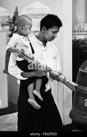 BURMESISCHE Mann mit Sohn klingelt an der SHWEDAGON PAYA oder Pagode, die stammt aus der Zeit des Buddha - YANGON, BIRMA Stockfoto