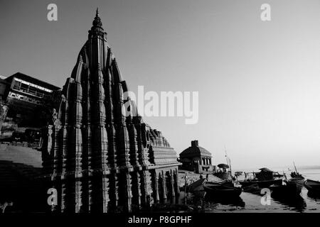 Ein Hindu Tempel erhebt sich über Kanus auf dem GANGES - VARANASI (Benares), Indien Stockfoto