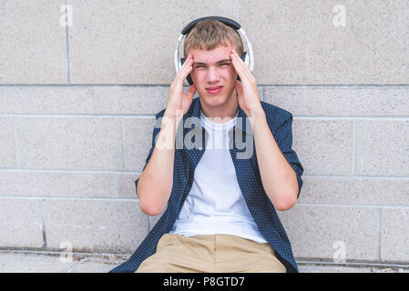 Mit Kopfschmerzen Musik hören, während auf dem Boden sitzend gegen eine Wand jugendlich. Stockfoto