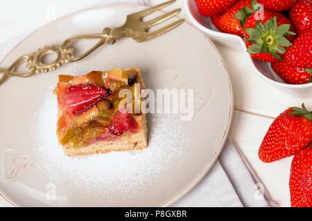 Stück Erdbeeren und Rhabarber Torte serviert auf rustikale Platte mit Messing Gabel und frische Erdbeeren Stockfoto