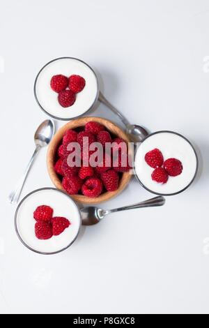 Top down Sicht auf drei Tassen Joghurt mit Löffel um Holz- Schale mit frischen Himbeeren angeordnet Stockfoto