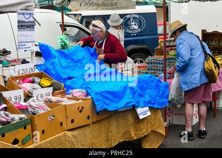 Axminster, Devon, Großbritannien. 12. Juli 2018. UK Wetter. Ein Markt Inhaber stall deckt seine Waren mit einer Plane in der Stadt Vina Del Mar in Devon als Licht auf eine warme Dusche am Morgen bedeckt. Foto: Graham Jagd-/Alamy leben Nachrichten Stockfoto