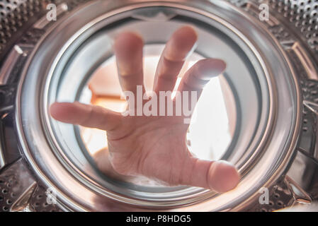 Eine Hand ist das Erreichen der Kleidung in die Waschmaschine. Stockfoto