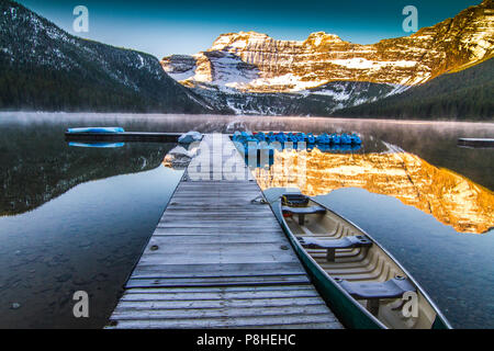 Cameron Lake im Morgenlicht mit hölzernen Pier und Kanu, mit mountaiin Reflexionen in See. Waterton National Park, Alberta, Kanada Stockfoto