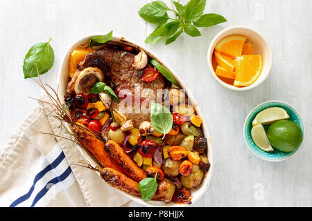 Reisgericht mit Rindfleisch gebacken mit Gemüse (Kartoffeln, Karotten, Aubergine, Zucchini und Tomate) in Keramik Topf auf hölzernen weißen Hintergrund mit Basilikum Sauce Stockfoto