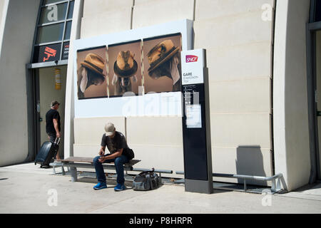 Avignon, Frankreich. TGV und Eurostar Bahnhof. Ein Fahrgast wartet unter einem Plakat der Hunde Hüte tragen von William Wegman aus seiner Ausstellung "H Stockfoto