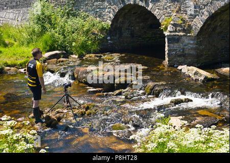 Man Fotos mit Kamera auf Stativ aus dem 18. Jahrhundert Brücke über den Fluss Dart in Dartmoor bei Postbridge Devon England Großbritannien Stockfoto
