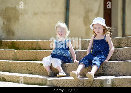 Zwei süße kleine Schwestern sitzen auf der Treppe im Freien Stockfoto