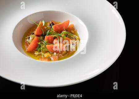 Eine köstliche Vorspeise aus Lachs, Tomatenscheiben, Kräutern und Gewürzen in einer Sauce serviert. Stockfoto