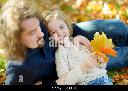 Junger Vater und seine kleine Tochter sitzen auf gelb Ahornblätter auf schönen sonnigen Herbsttag Stockfoto