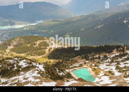 Ein Blick von Oben auf die Berge und Hügel zwischen zwei Seen, von einem dichten Nadelwald und Landstraßen, Schnee auf dem Gipfel des Berges umgeben Stockfoto