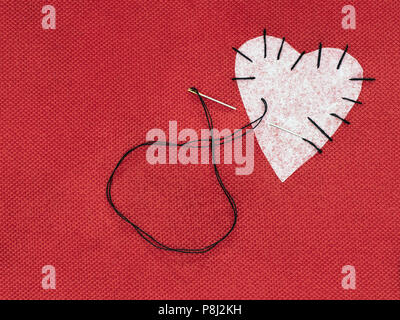 Stoff Herz rot mit weissen Flecken und schwarzem Nähgarn. Gebrochenes Herz Konzept ausbessern. Stockfoto
