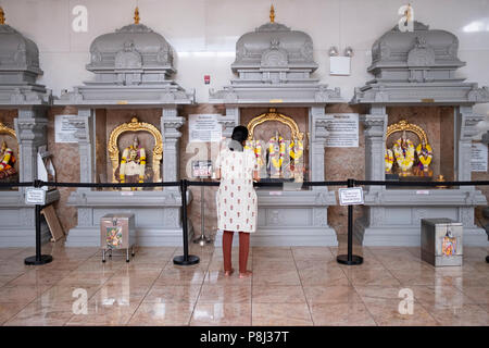 Eine Frau betend und meditierend vor Statuen der Götter und Göttinnen im hinduistischen Tempel Gesellschaft in Flushing, Queens, New York City. Stockfoto