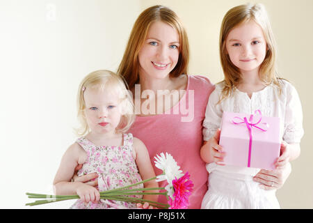 Junge Mutter und ihre kleine Tochter ein Geschenk in rosa Geschenkpapier und Blumen verpackt Stockfoto