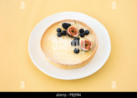 Lemon tart in Scheiben geschnitten und mit frischen Feigen, Heidelbeeren und Brombeeren auf hellgrauem Hintergrund mit Kopie Raum eingerichtet. Ansicht von oben. Stockfoto