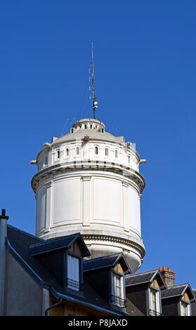 Blick auf den ikonischen Wasserturm in Montmartre, Paris, hinter einem Haus Dach mit drei Giebeln und vor blauem Himmel. Stockfoto