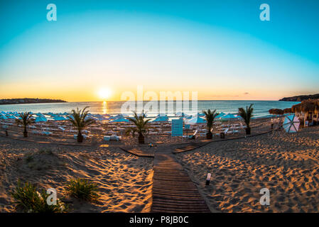 Sonne am Horizont leuchtet Holzsteg über die Sanddünen zu wilden Strand Stockfoto