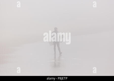 DEAL, NEW JERSEY - April 28, 2018: ein Surfer am Strand spazieren auf einem sehr neblig Frühling Morgen Stockfoto