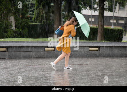 Belgrad, Serbien - Juni 14, 2018: Eine junge Frau unter dem Dach in der plötzliche schwere Feder windig Regen in der Stadt Park läuft, hält eine Flasche Stockfoto