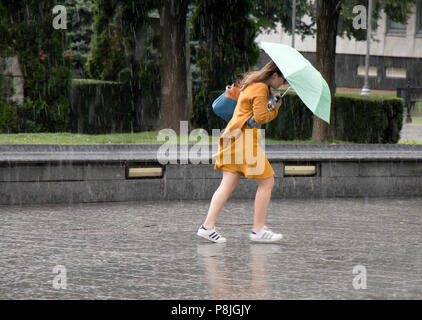 Belgrad, Serbien - Juni 14, 2018: Eine junge Frau unter dem Dach in der plötzlichen schweren und windigen Frühjahr Regen in der Stadt Park läuft, hält ein Bott Stockfoto