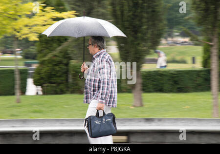 Belgrad, Serbien - Juni 14, 2018: Ein mittleres Alter Mann unter dem Dach im Frühjahr Regen im Stadtpark, im Besitz einer Tasche Stockfoto