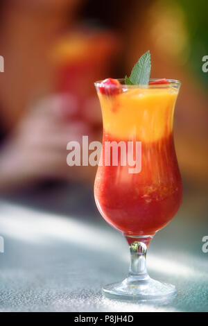 Virgin Strawberry Mango Margarita mocktail. Bunte alkoholfreien Cocktail, Fruit Smoothie trinken auf einem Tisch mit einer Frau mit einem Glas in der Stockfoto