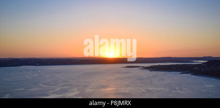 Die Sonne in einer Flamme von leuchtendem Orange, Rosa und Gelb über Lake Travis in das Gebirge zentrale Texas in der Nähe von Austin. Stockfoto