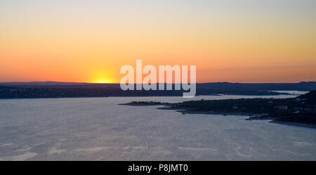 Die Sonne in einer Flamme von leuchtendem Orange, Rosa und Gelb über Lake Travis in das Gebirge zentrale Texas in der Nähe von Austin. Stockfoto