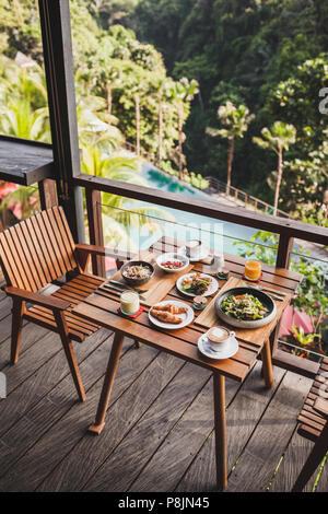 Tabelle mit Frühstück serviert auf hölzernen Terrasse mit Pool und Jungle View in Bali. Stockfoto