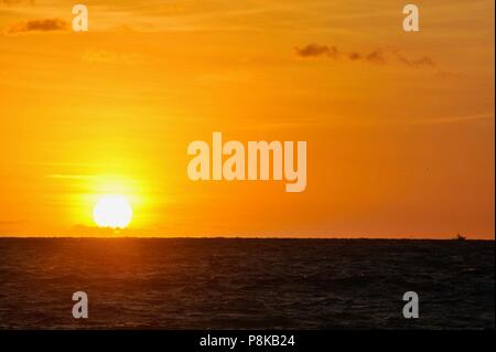 Bunte, teilweise bewölkt orange Sonnenuntergang mit Silhouette Charter Angeln Boot im Abstand Beschleunigung über den Atlantik aus Florida, USA gesehen. Stockfoto