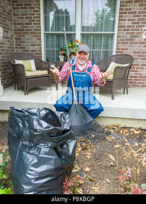 Glücklich Gärtner mit Harken die Blätter in seinem Garten auf seiner Veranda und deutete mit der Hand in die Kamera grinsen beendet Stockfoto