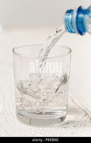 Das Gießen von Wasser aus einer Flasche in ein Glas. Weiß Holz Hintergrund. Stockfoto