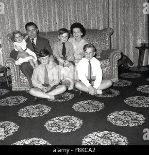 1950er Jahre, Familie zu Hause, Vater und Mutter mit ihren drei Jungen und junge Kind togetther sitzen auf dem Sofa in Ihrem Wohnzimmer mit einem unverwechselbaren gemusterten Teppich. Stockfoto