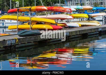 Bunte Kajaks auf einem Rack und deren Reflexionen im Westen Becken in Mamaroneck Hafen in Harbour Island Park, Mamaroneck, New York. Stockfoto