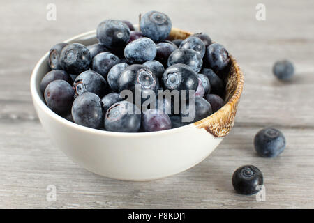 Kleine Schüssel voll von Blaubeeren, einige von ihnen auf grau Holz Schreibtisch verschüttet. Stockfoto