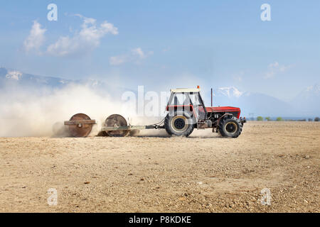 Tractor Pulling heavy metal Walzen, die Vorbereitung von Feld im Frühling, mit Bergen im Hintergrund. Stockfoto