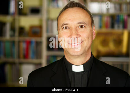 Das Porträt einer gut aussehenden lächelnd katholischen Priester. Er schaut uns mit Interesse, Nachdenklichkeit, Missionierung, Freude, Glück und Frieden. Stockfoto