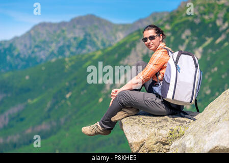 Frau Wanderer mit einem Rucksack in den Bergen sitzt auf einem Felsen Stockfoto