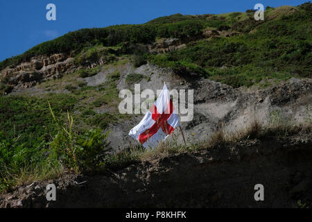 Die verräterische bis in die Hütten und Almen am alten Hafen von Port Mulgrave auf der Yorkshire Heritage Coast, England, UK, englische Flagge. Stockfoto