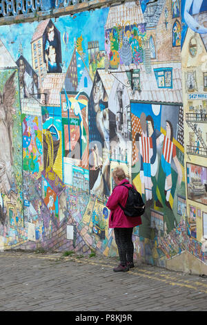 Ältere Menschen, Rentner lady Phone gegen Streetart, Graffiti Wand auf gepflasterten Straße von blands Klippe, Yorkshire Ferienort Scarborough, Großbritannien Stockfoto