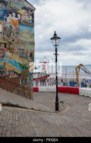 Alte Strassenlaterne und Gebäude mit street art auf der Seite mit Blick auf das Meer mit neuen Gebäude nur in Bild bei Scarborough, North Yorkshire, Großbritannien gebaut Stockfoto