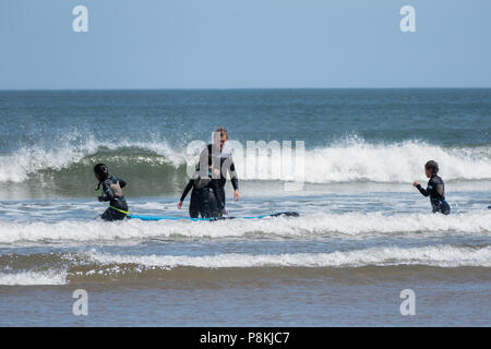 Gruppe von vier Spaß genießen, im Meer mit großen Wellen am Strand von North Bay, Scarborough, Yorkshire, Großbritannien, Stockfoto