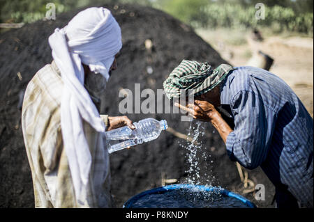 Juli 11, 2018 - Gaza, Gaza, Palästina, Palästinensische holzkohle workerMohammed Abu Khater reinigt sein Gesicht mit Wasser mit Hilfe seines Kollegen im Al Habbash Produktionsstätte, östlich der Flüchtlingslager Jabaliya, Northern Gaza, Gazastreifen, 11. Juli 2018. Die Al Habbash Kohle-machen ist das größte Hersteller in den Gazastreifen. Sieben Männer Arbeit während des ganzen Jahres, besonders im Winter und Urlaub Zeiträume, in denen die Kohle ist in der hohen Nachfrage. Während die Arbeiter, die verschiedenen Arten der Bäume schneiden, Brennholz ist in der Regel verwendet, um Kohle zu machen. Die Zitrusfrüchte ist sehr nützlich und die Stockfoto