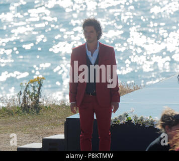 Newquay, Cornwall, England. 12. Juli 2018. Rosamunde Pilcher Schauspieler Manuel Mairhoffer spielt Klavier auf den Klippen, Filmen 'Meine Brüder Braut' Fistral Beach, UK, 12., Juli, 2018 Robert Taylor/Alamy Leben Nachrichten. Newquay, Cornwall, England. Credit: Robert Taylor/Alamy leben Nachrichten Stockfoto