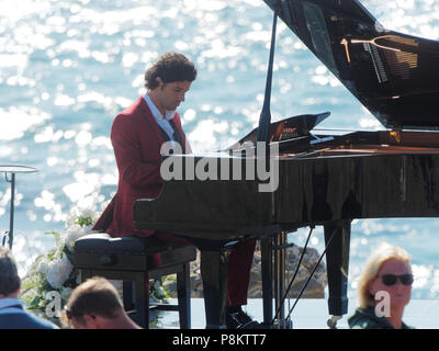 Newquay, Cornwall, England. 12. Juli 2018. Rosamunde Pilcher Schauspieler Manuel Mairhoffer spielt Klavier auf den Klippen, Filmen 'Meine Brüder Braut' Fistral Beach, UK, 12., Juli, 2018 Robert Taylor/Alamy Leben Nachrichten. Newquay, Cornwall, England. Credit: Robert Taylor/Alamy leben Nachrichten Stockfoto