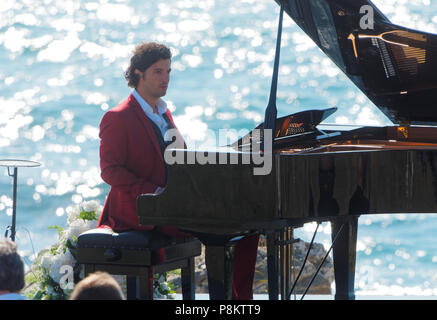 Newquay, Cornwall, England. 12. Juli 2018. Rosamunde Pilcher Schauspieler Manuel Mairhoffer spielt Klavier auf den Klippen, Filmen 'Meine Brüder Braut' Fistral Beach, UK, 12., Juli, 2018 Robert Taylor/Alamy Leben Nachrichten. Newquay, Cornwall, England. Credit: Robert Taylor/Alamy leben Nachrichten Stockfoto