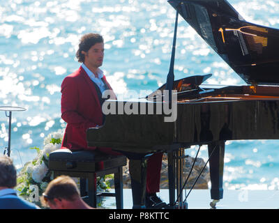 Newquay, Cornwall, England. 12. Juli 2018. Rosamunde Pilcher Schauspieler Manuel Mairhoffer spielt Klavier auf den Klippen, Filmen 'Meine Brüder Braut' Fistral Beach, UK, 12., Juli, 2018 Robert Taylor/Alamy Leben Nachrichten. Newquay, Cornwall, England. Credit: Robert Taylor/Alamy leben Nachrichten Stockfoto