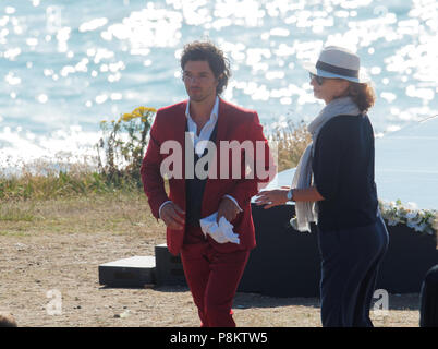 Newquay, Cornwall, England. 12. Juli 2018. Rosamunde Pilcher Schauspieler Manuel Mairhoffer spielt Klavier auf den Klippen, Filmen 'Meine Brüder Braut' Fistral Beach, UK, 12., Juli, 2018 Robert Taylor/Alamy Leben Nachrichten. Newquay, Cornwall, England. Credit: Robert Taylor/Alamy leben Nachrichten Stockfoto