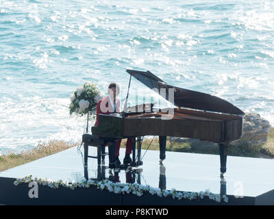 Newquay, Cornwall, England. 12. Juli 2018. Rosamunde Pilcher Schauspieler Manuel Mairhoffer spielt Klavier auf den Klippen, Filmen 'Meine Brüder Braut' Fistral Beach, UK, 12., Juli, 2018 Robert Taylor/Alamy Leben Nachrichten. Newquay, Cornwall, England. Credit: Robert Taylor/Alamy leben Nachrichten Stockfoto