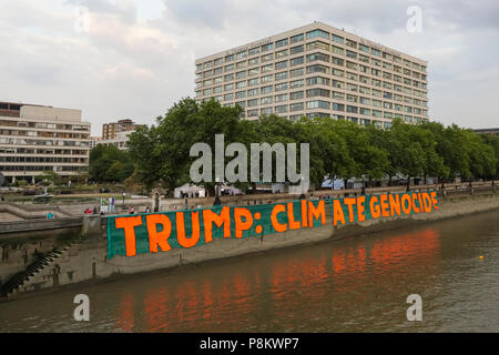 Westminster, London, 12. Juli 2018. Aktivisten gegen den Klimawandel Protest gegen Donald Trump besuchen, indem sie einen riesigen Banner lesen "Trumpf: Klima Völkermord" in St Thomas' Hospital Gärten, gegenüber dem Parlament in Westminster. Die riesigen Banner, 100 Meter x 9 Meter groß, ist es, das Bewusstsein über die US-Präsidenten Klimapolitik zu erhöhen. Credit: Imageplotter Nachrichten und Sport/Alamy leben Nachrichten Stockfoto